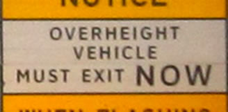 The photograph at lower right is a rectangular regulatory sign that displays the legend "OVERHEIGHT VEHICLES MUST EXIT NOW" in the alternative alphabet in a negative-contrast orientation.